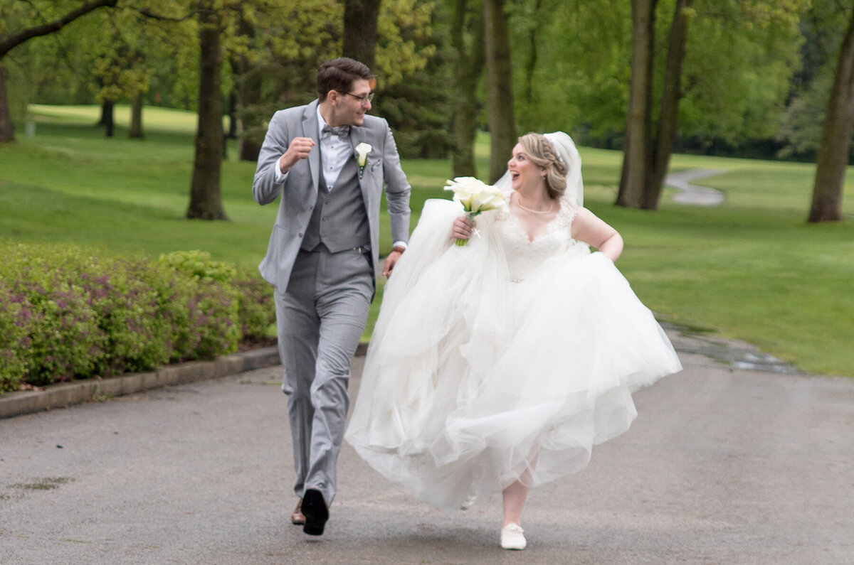 Bride and groom joyfully run through a park