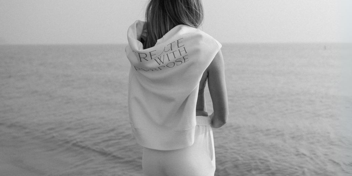 Marketing Agency Brand Photos, Woman standing infront of Lake Michigan with Sweatshirt on shoulders that reads "Create with Purpose" Social Media Agency