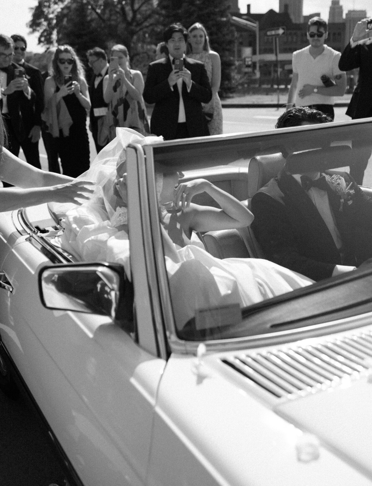 a guest helps a bride fit her long veil in a vintage convertible in Detroit, Michigan