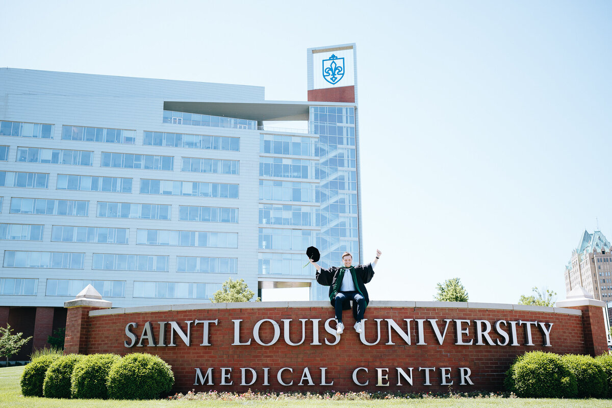 slu med school graduate sitting on school sign
