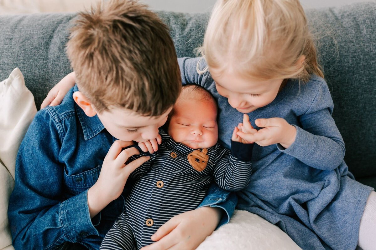 Siblings kiss the hands of their baby brother.