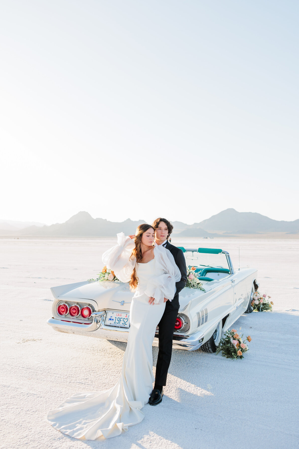 bride and groom posing in front of a car in the Utah saltflats