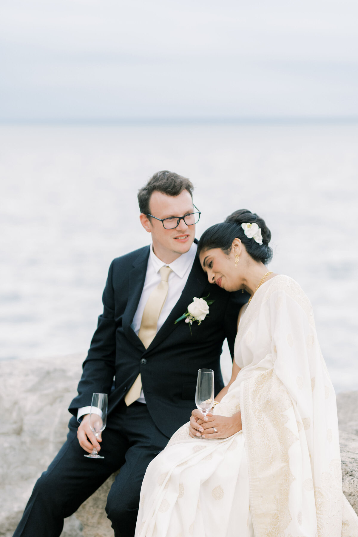 Bride lays her head on grooms shoulder with a glass of champagne in her hand