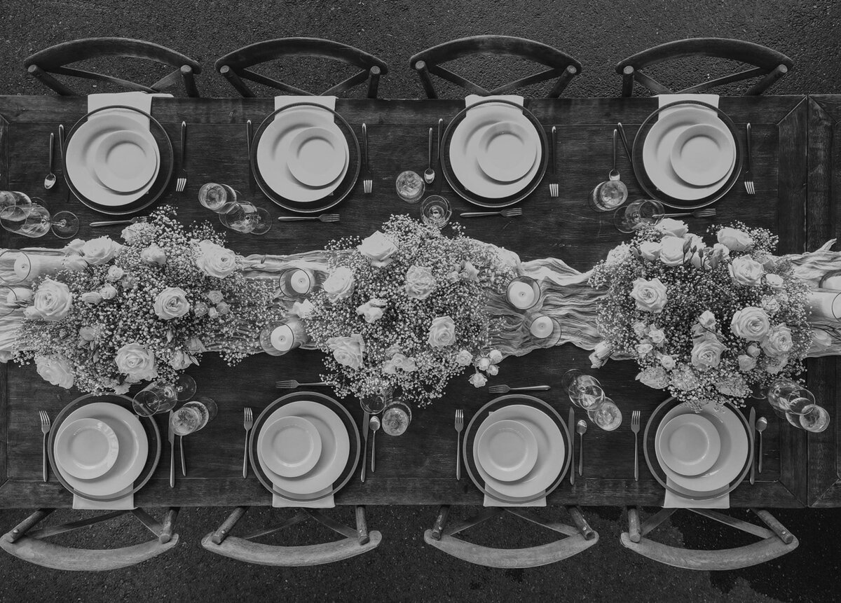 A black-and-white overhead view of a beautifully styled elopement dinner table with floral centerpieces, candles, and place settings arranged symmetrically, captured by Sydney Breann Photography.