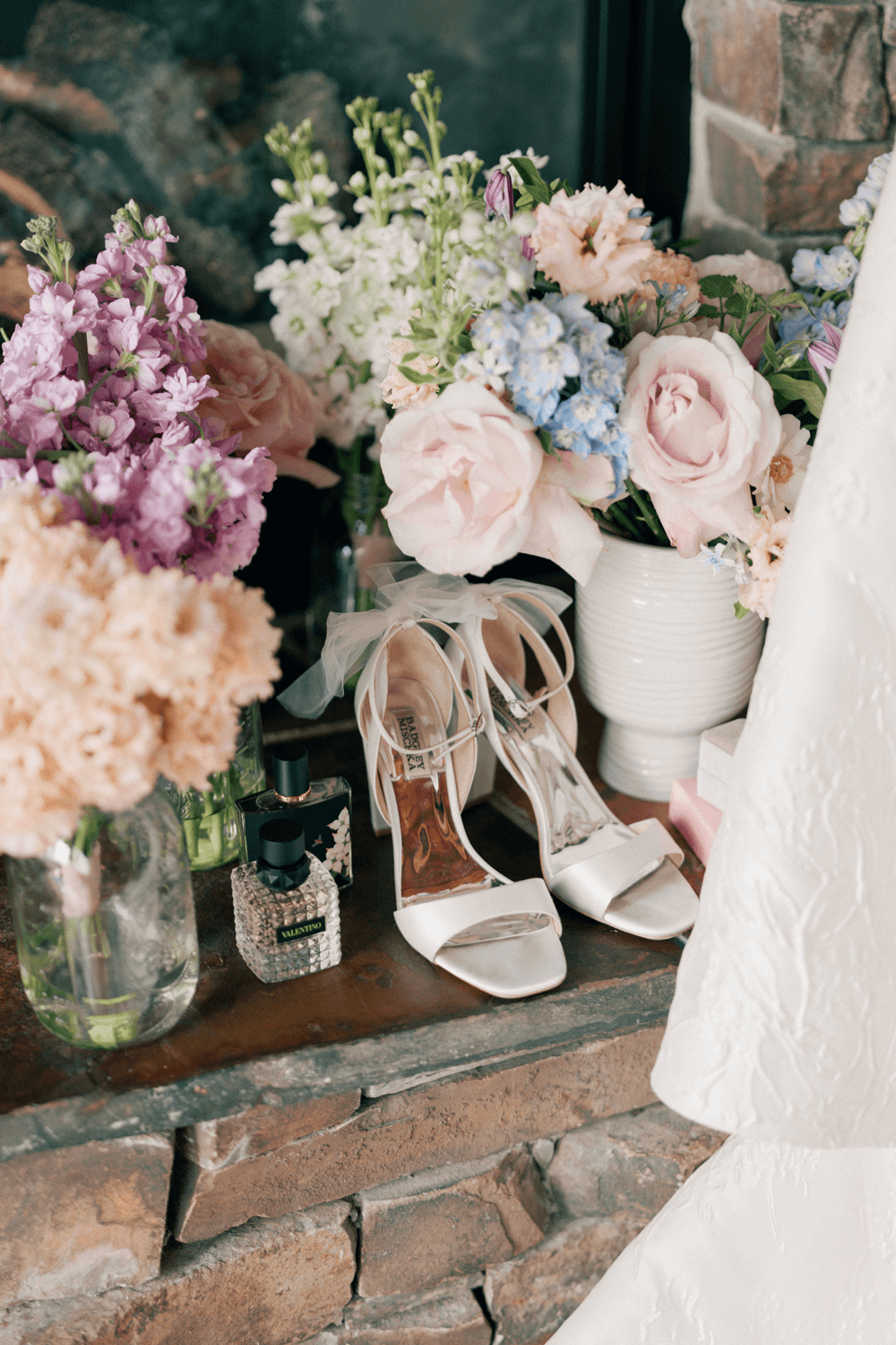 Bridal shoes, perfume, and pastel wedding bouquets styled on a stone hearth for a summer wedding at Moonlight Basin.