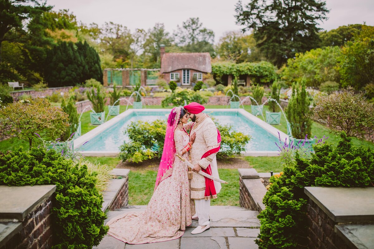 A sikh bride and groom touch foreheads at the planting fields arboretum near the pool in oyster bay, ny