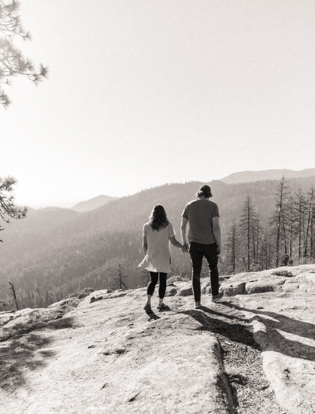 Couple holding hands and walking along rocky terrain with mountains in the background