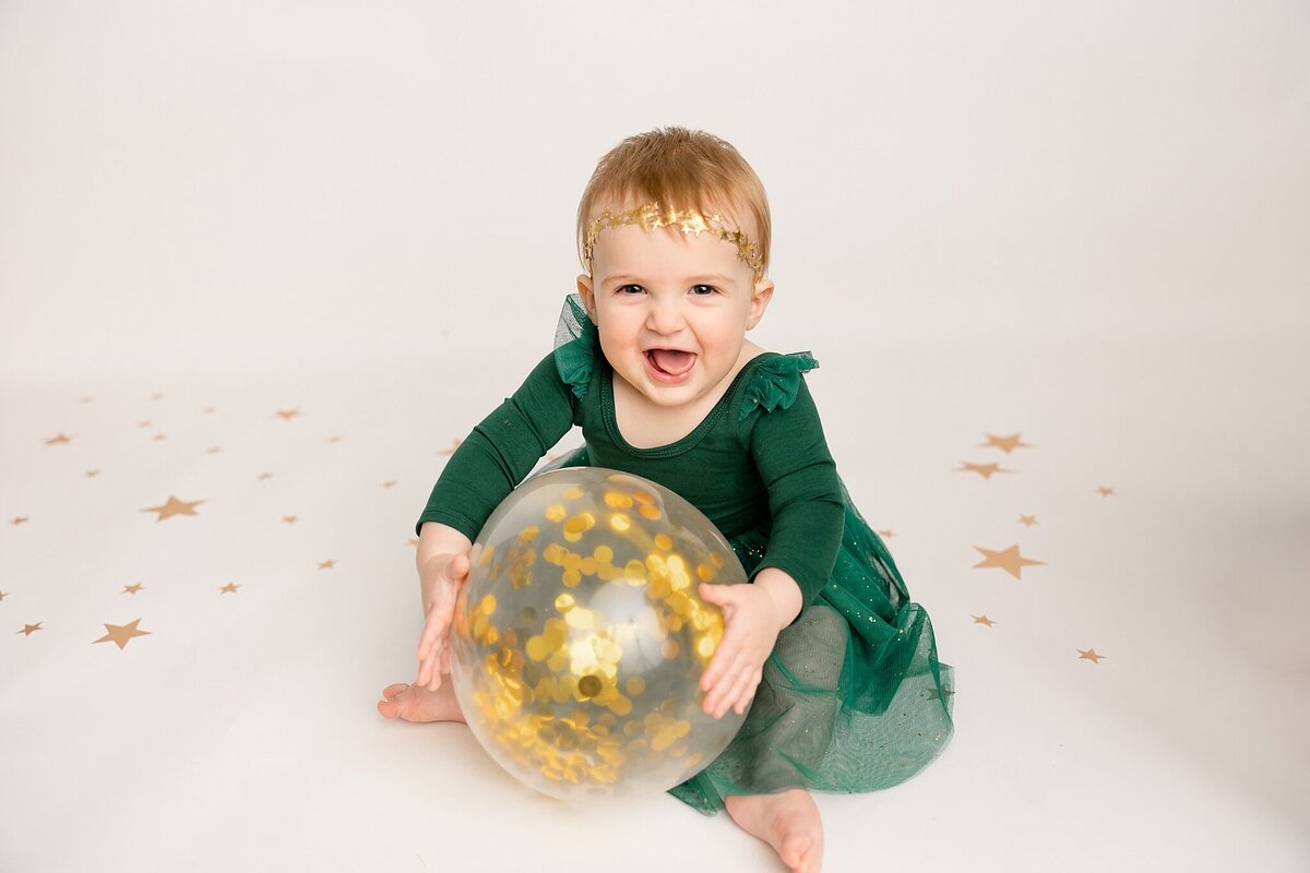 baby girl in green dress hugging confetti balloon in portland studio