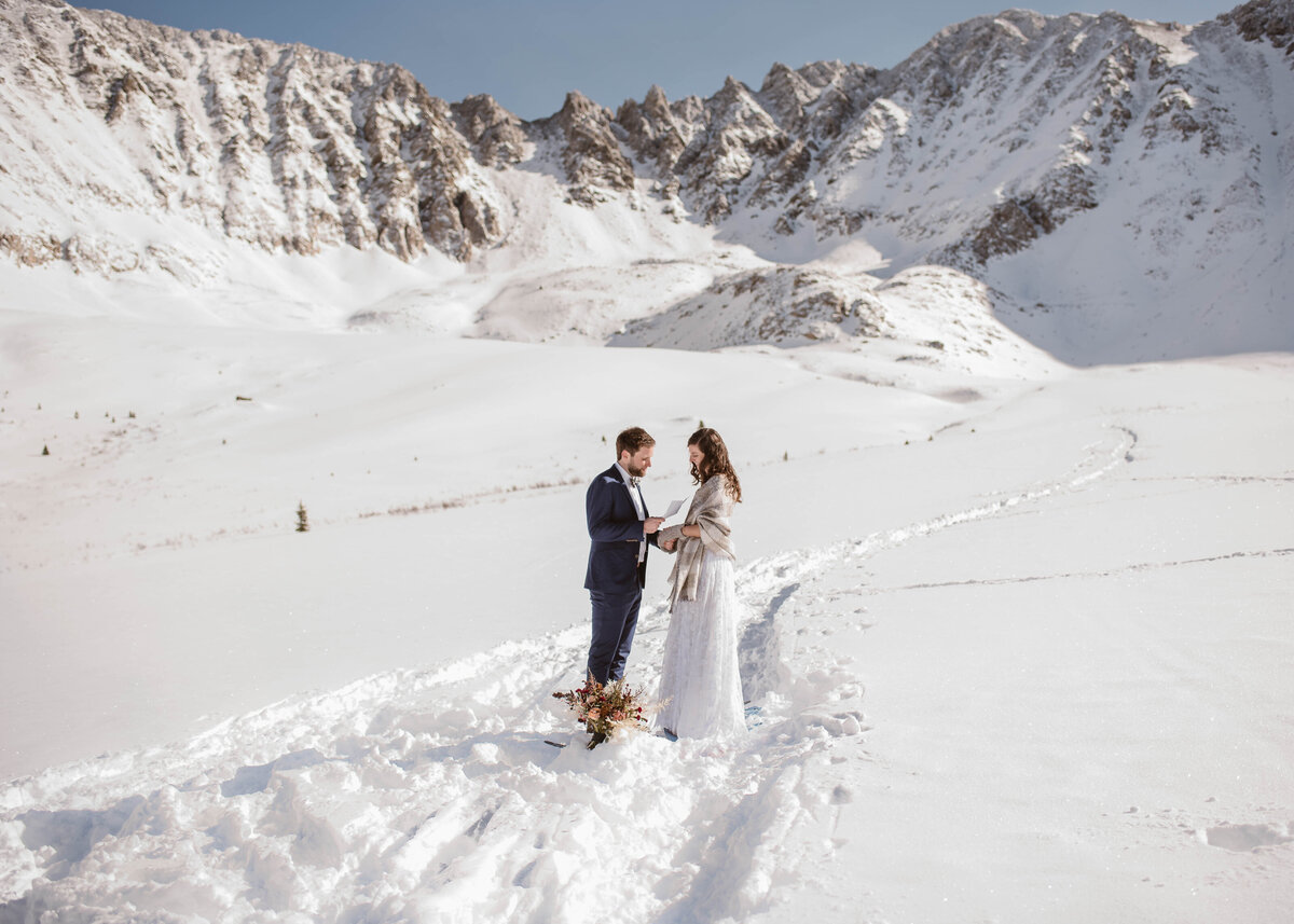 Bride and groom walk through a snow-dusted meadow surrounded by mountains during their Mayflower Gulch, Colorado elopement.