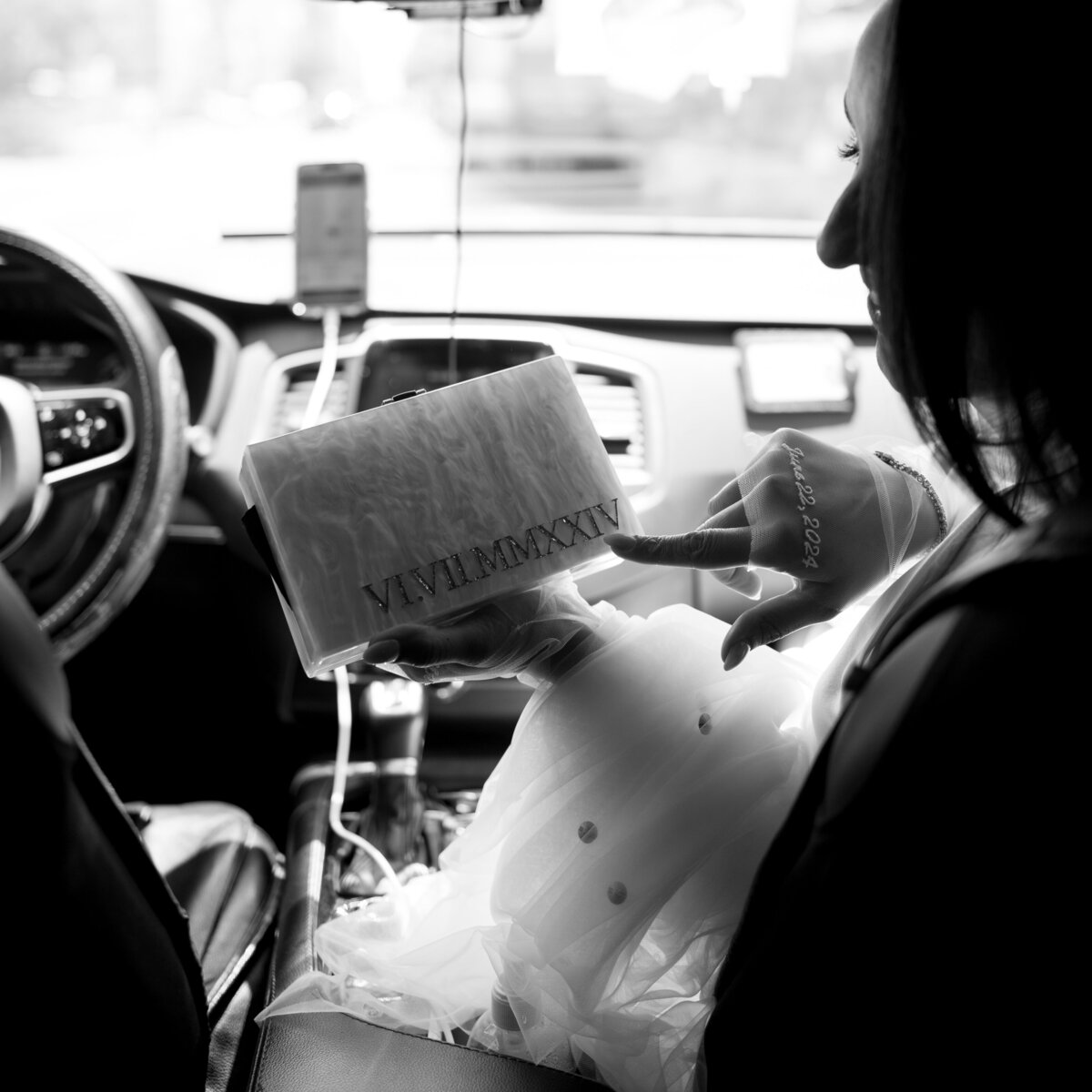 Black and white photo of the bride holding a custom wedding keepsake while riding in a New York City taxi, captured during Japna and Chris’s Hotel Chelsea elopement by NYC wedding photographer Perry Hancock.