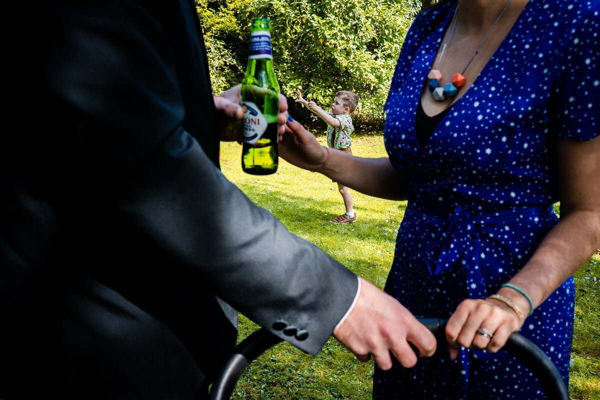 A child in the distance jumping in the air with arms out, making him look like he is trying to grab the bottle of peroni being held in the foreground.