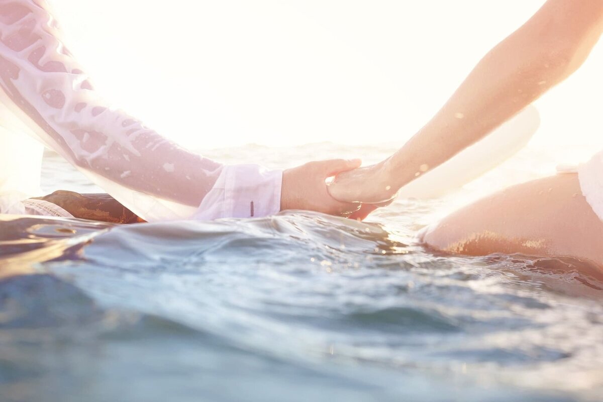 Surfing couple hold hands while on their surfboards after a water wedding in Maui, Hawaii