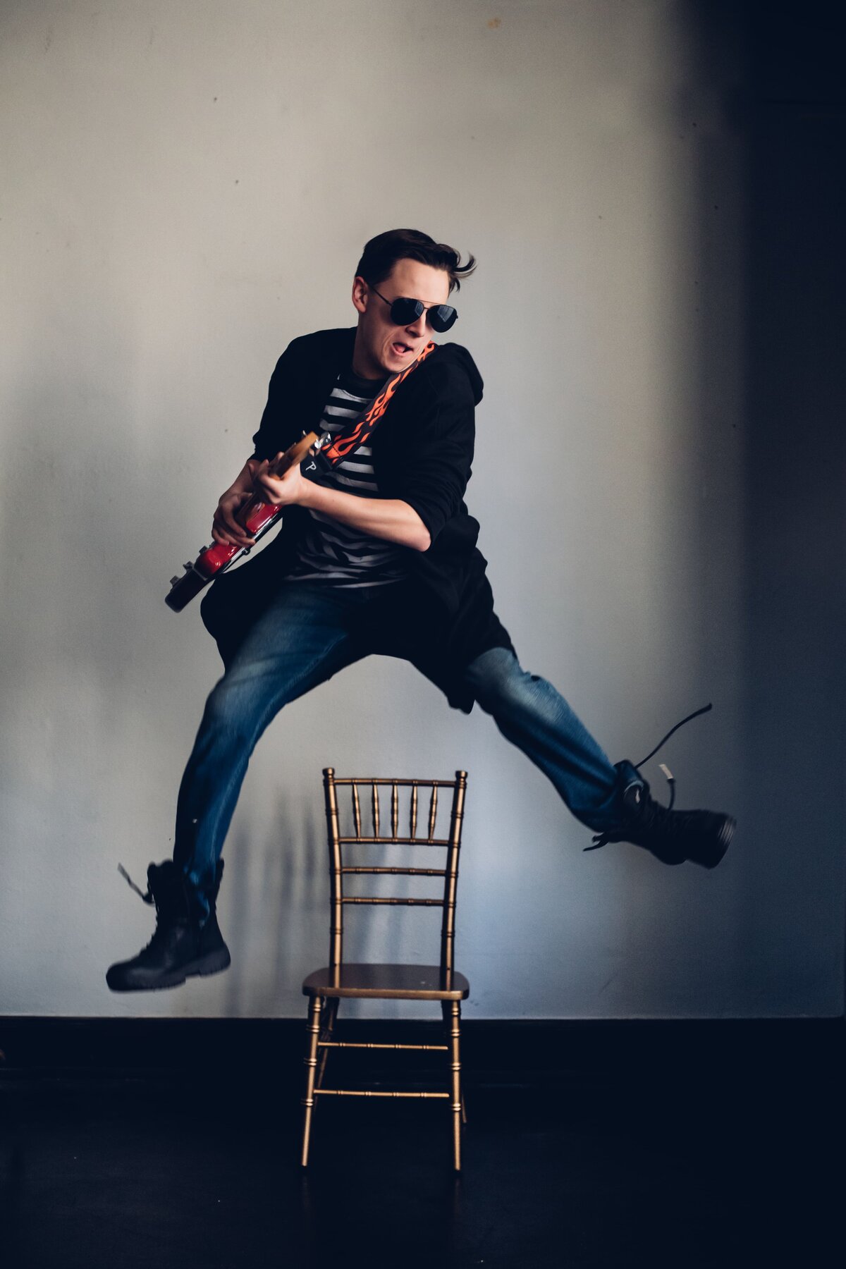 A young man jumping over a chair with a guitar, captured by Senior portrait photographer Britt Elizabeth