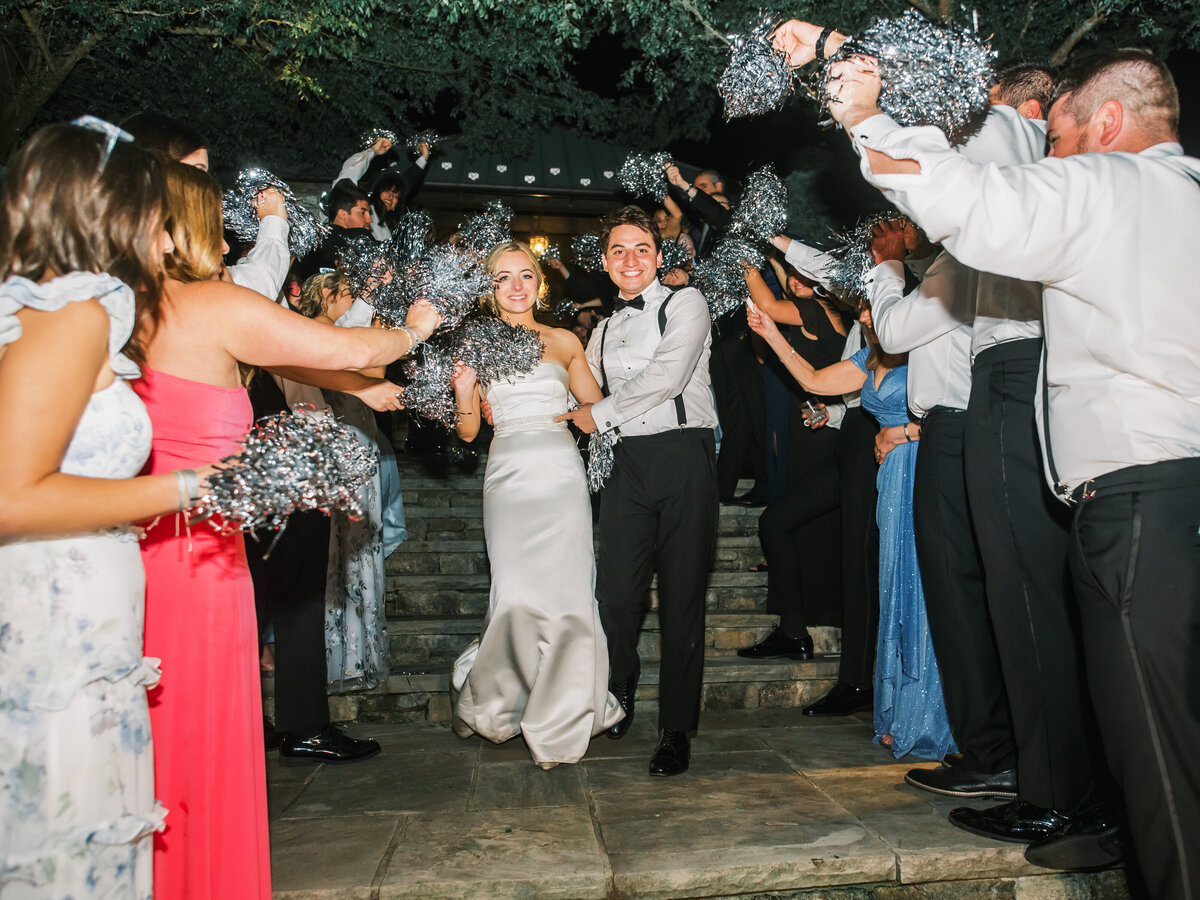 Bride and groom walking through a grand exit tunnel while guests cheer with pom poms at Old Edwards Inn in Highlands, North Carolina.
