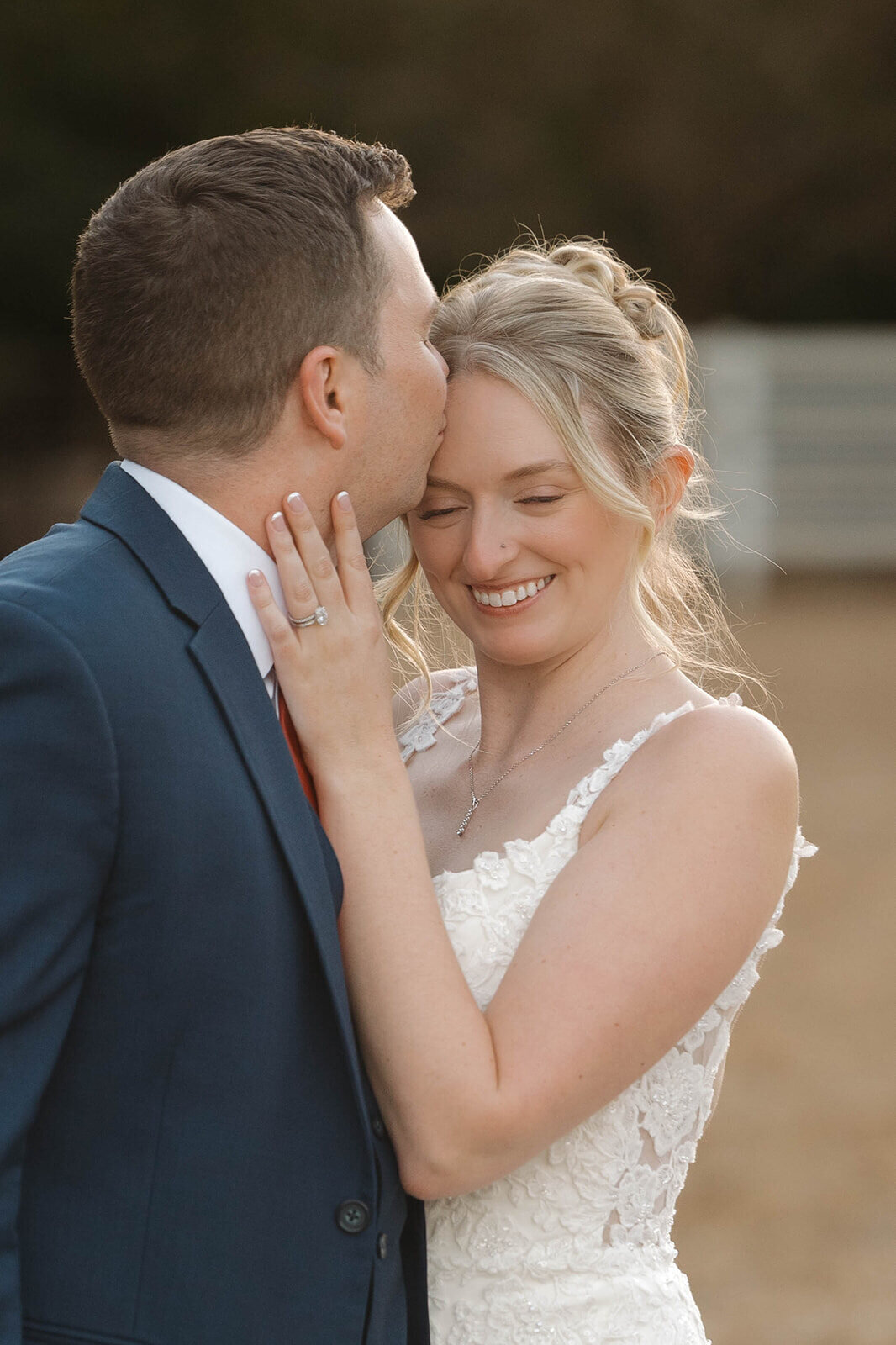 Groom kissing his bride on the forehead at sunset