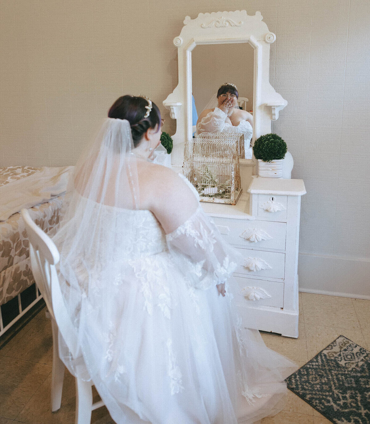 A bride places her hand over her mouth in excitement while looking in the mirror before her outdoor wedding.