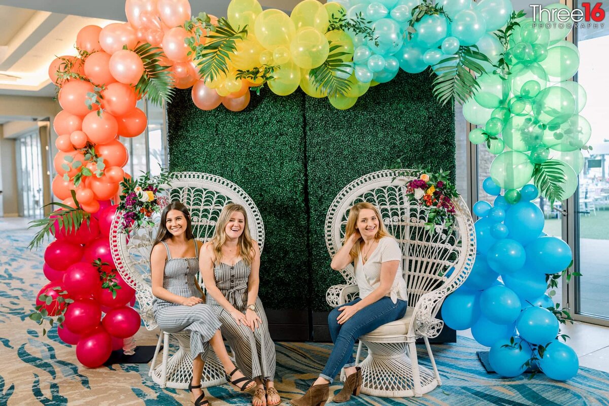 Ladies sit in chairs under a balloon arch as they prepare for an event