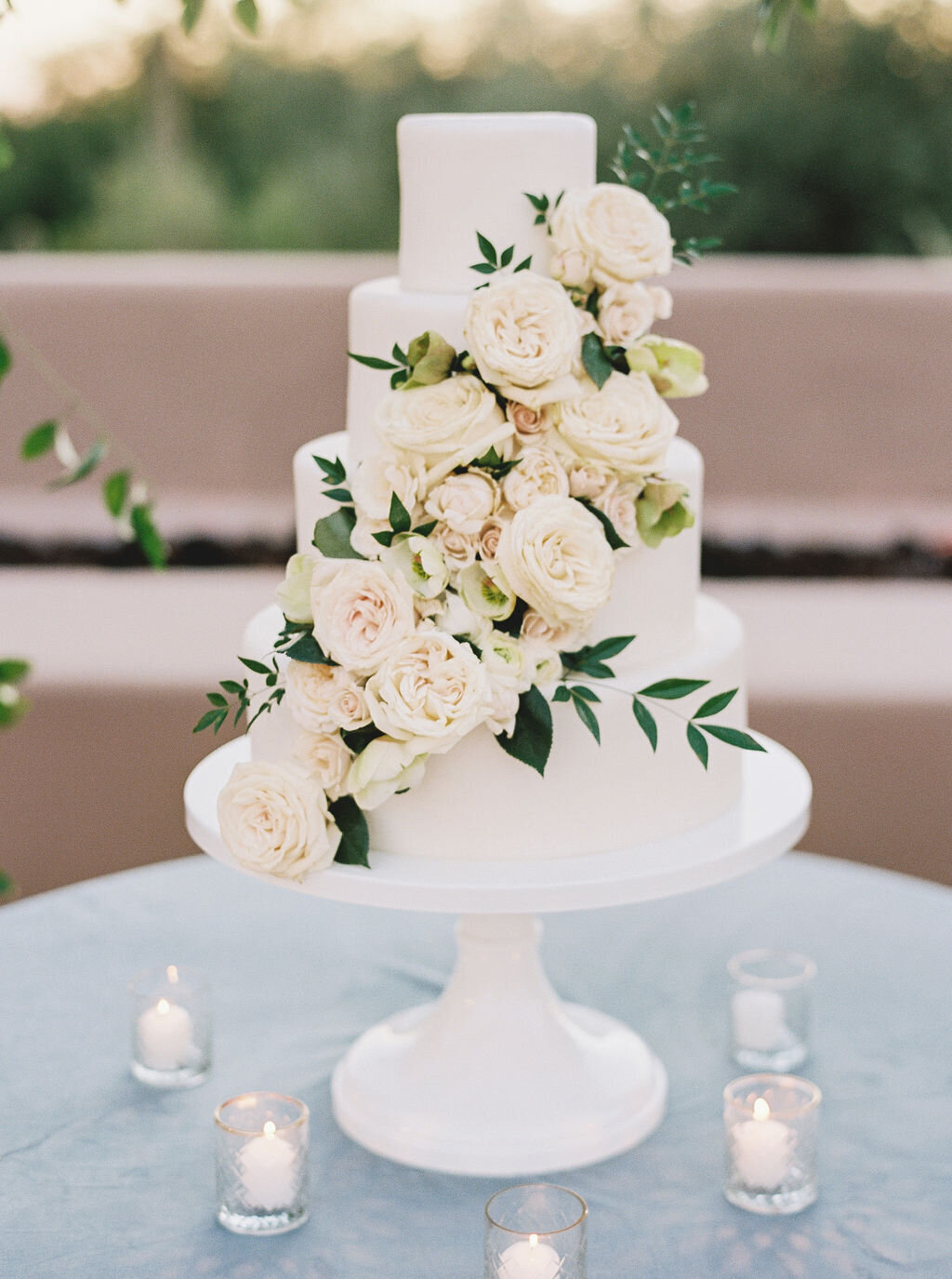 A beautifully designed white wedding cake adorned with cascading fresh roses, perfect for a romantic wedding reception.