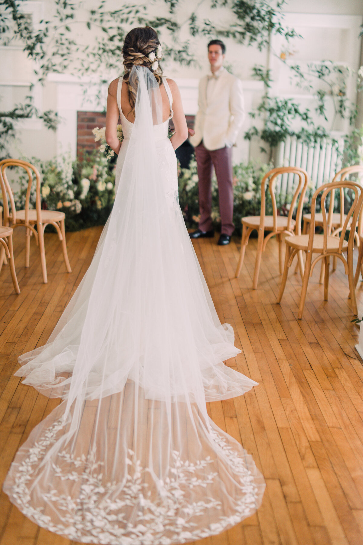 Bride processing down aisle  wearing Alexandra Grecco Marcelle gown & Ainsley veil to meet groom in white tuxedo in vine-covered room