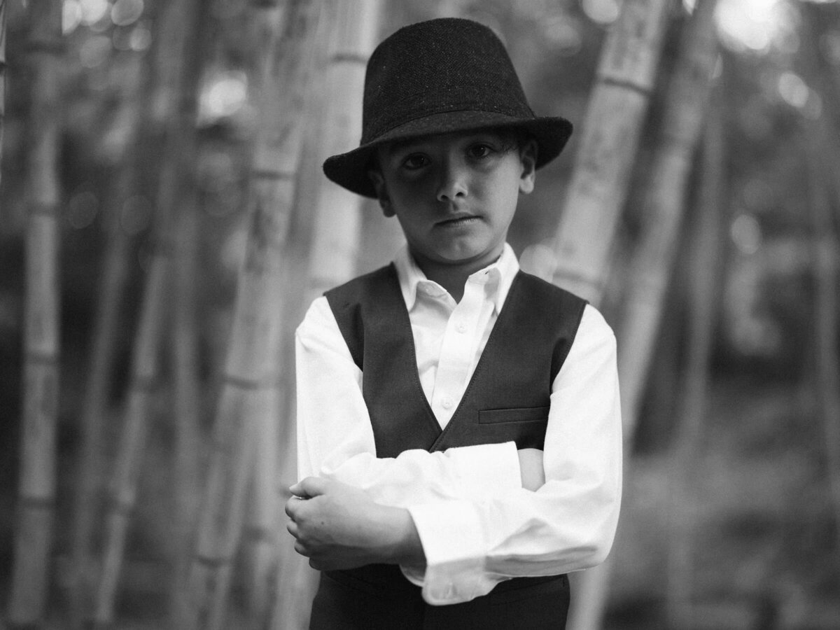 A small boy in a hat and suit with his arms crossed in front of him.