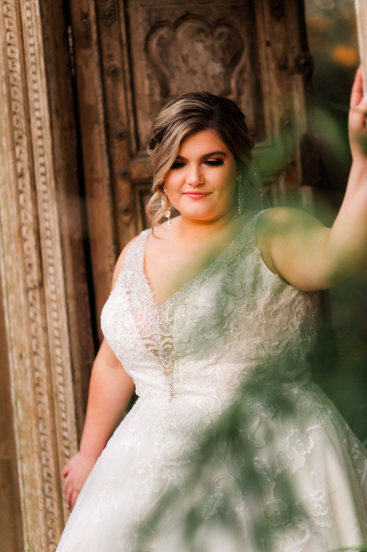 bride walking through an outdoor stone gate while holding onto the sides of the doorway and looking down captured by little rock wedding photographer