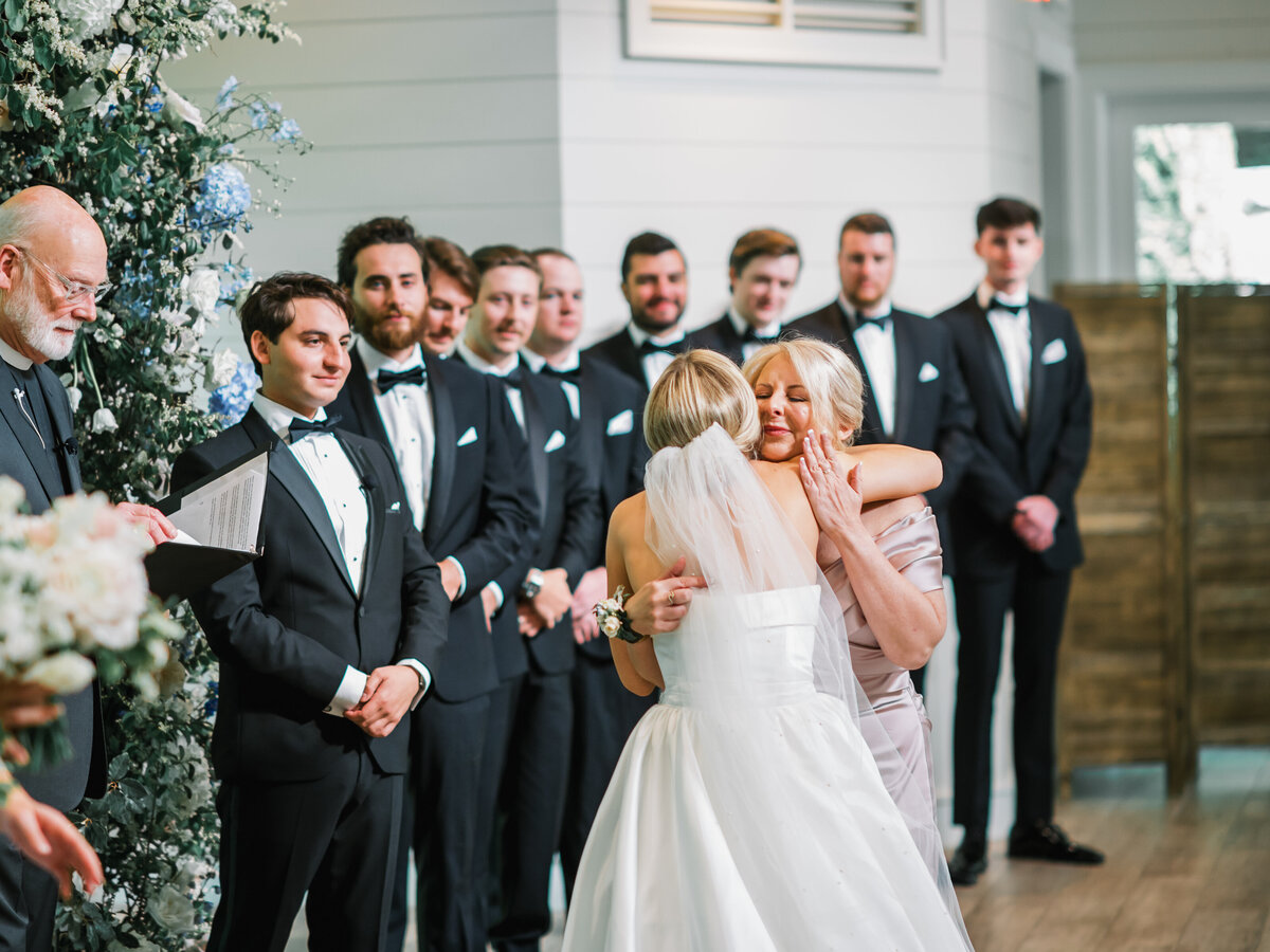 Emotional moment during the wedding ceremony as the bride shares a hug at the altar, surrounded by floral décor and groomsmen at Old Edwards Inn in Highlands, North Carolina.