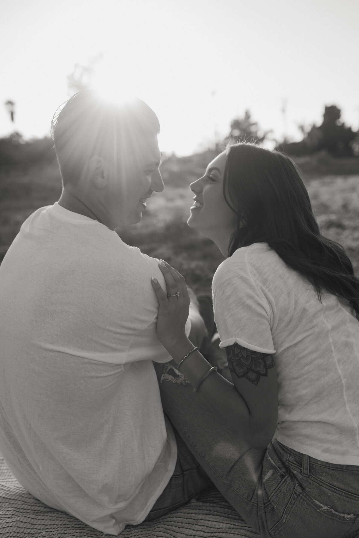 couple sitting together on picnic blanket in field leaning into each other laughing