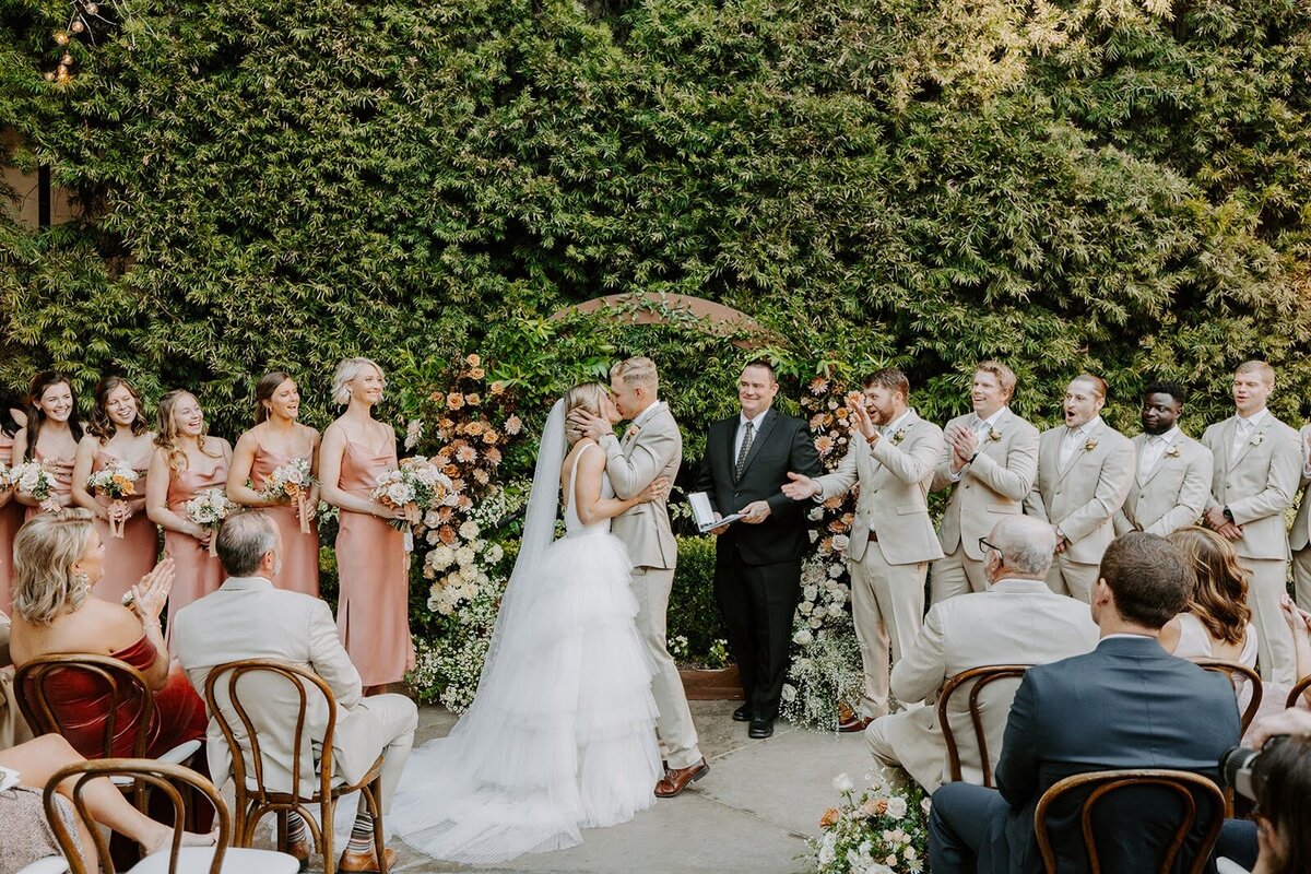 Bride and groom kissing in front of a circle arch at Franciscan Gardens