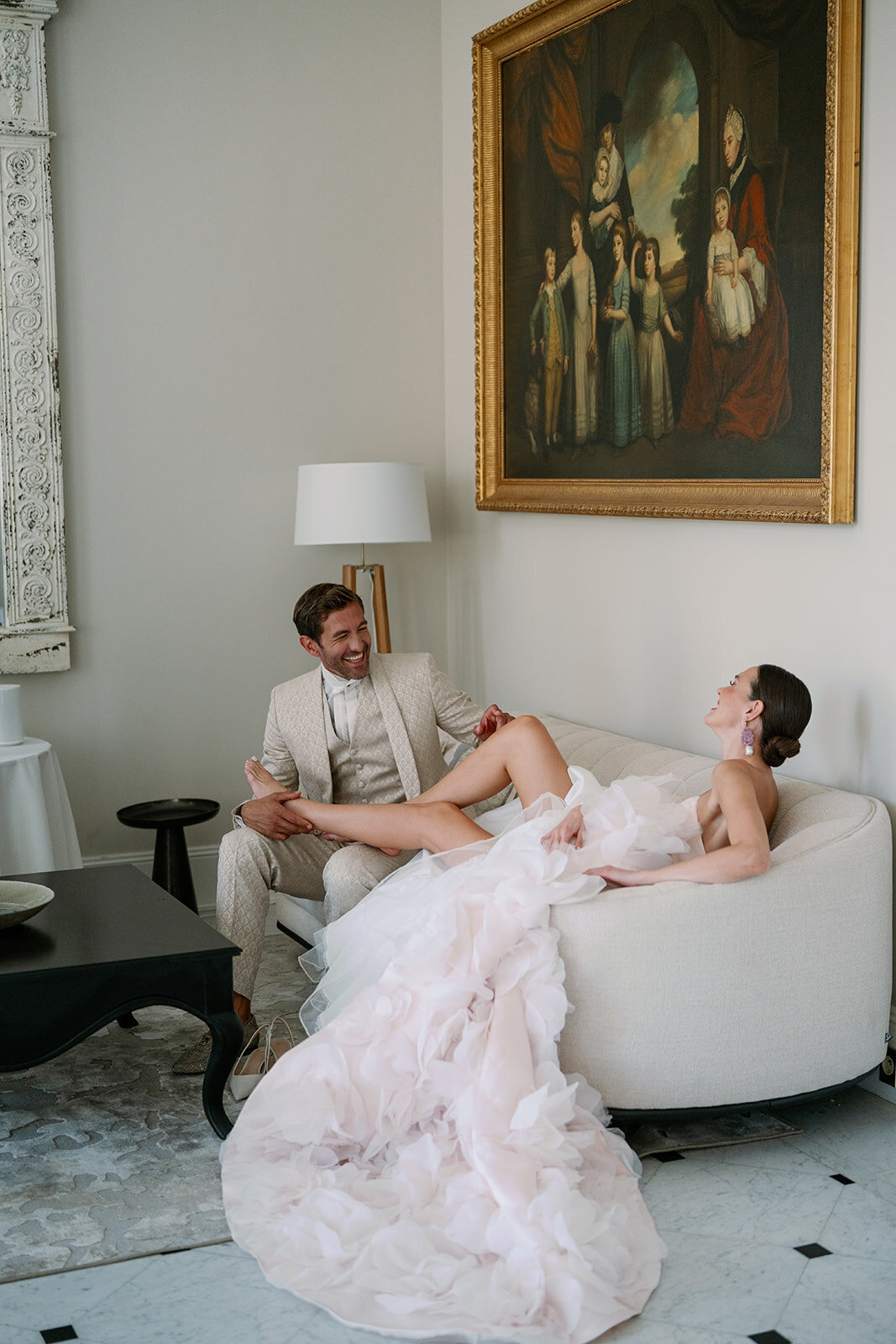 Bride and groom relaxing together in a French sitting room featuring artwork and luxury furniture at Château de Tourreau.