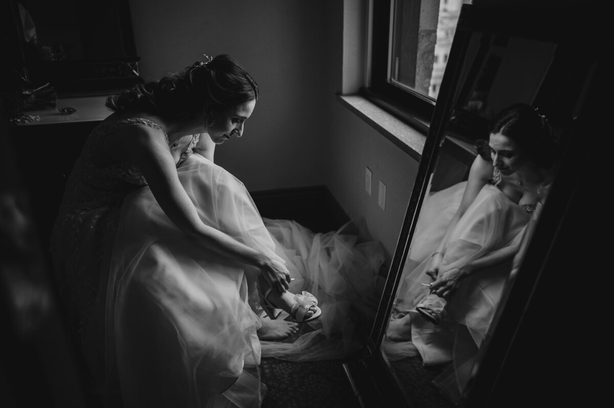 A bride is reflected  in a mirror while putter on her shoes