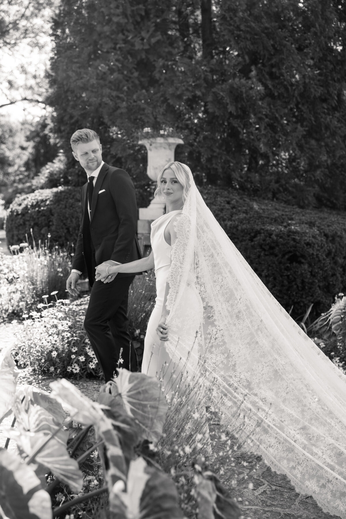 Bride glances back smiling as she walks with groom at Dayton garden wedding, Philadelphia photographer capture.