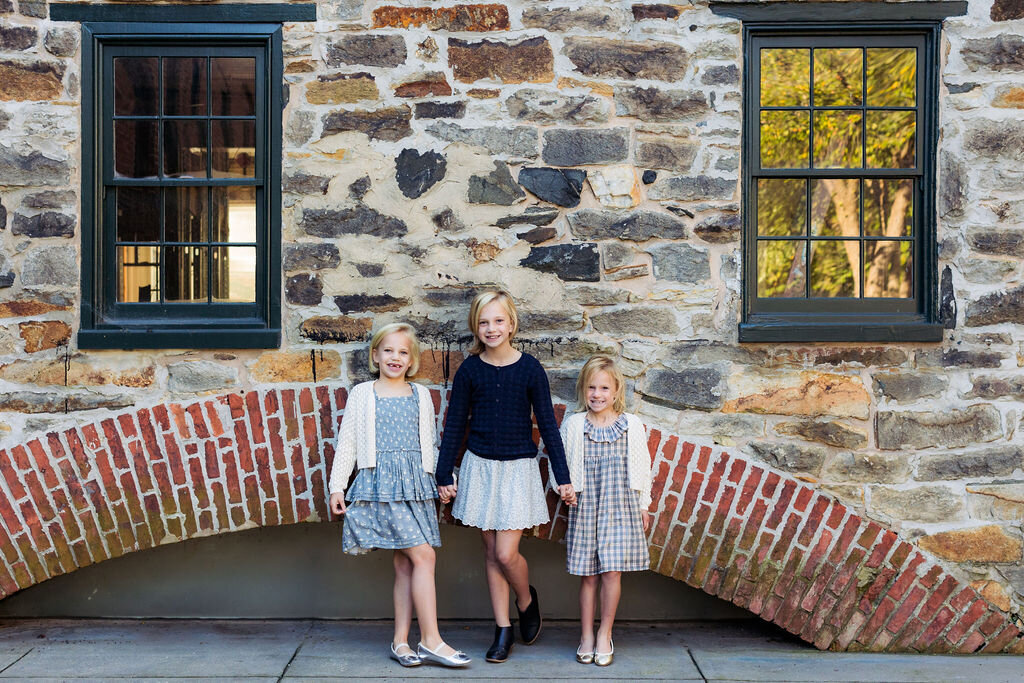 Three children all smile in front of a brick wall.
