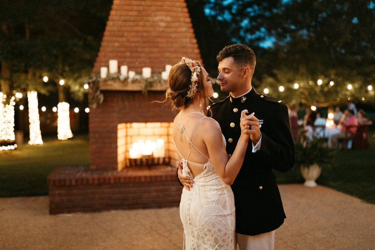 Boho bride with flower crown dancing with military groom in uniform on a patio with a candlelit fireplace in a backyard wedding
