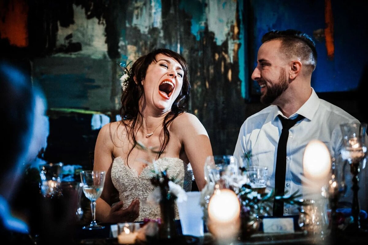 A wedding couple laughing while sitting at a table.