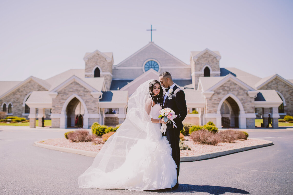 Indian christian malayali bride and groom in a white dress share a moment in front of the st. kateri tekakwitha church in new york