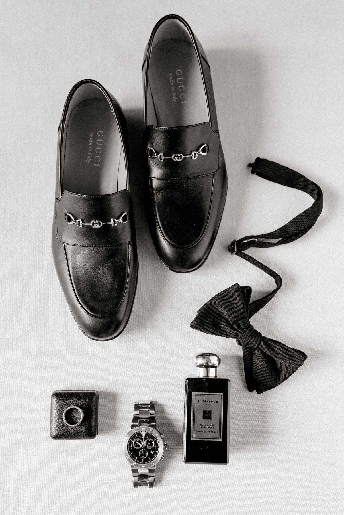 Groom's shoes, bowtie, cologne, watch and ring styled beautifully on a flat lay mat.