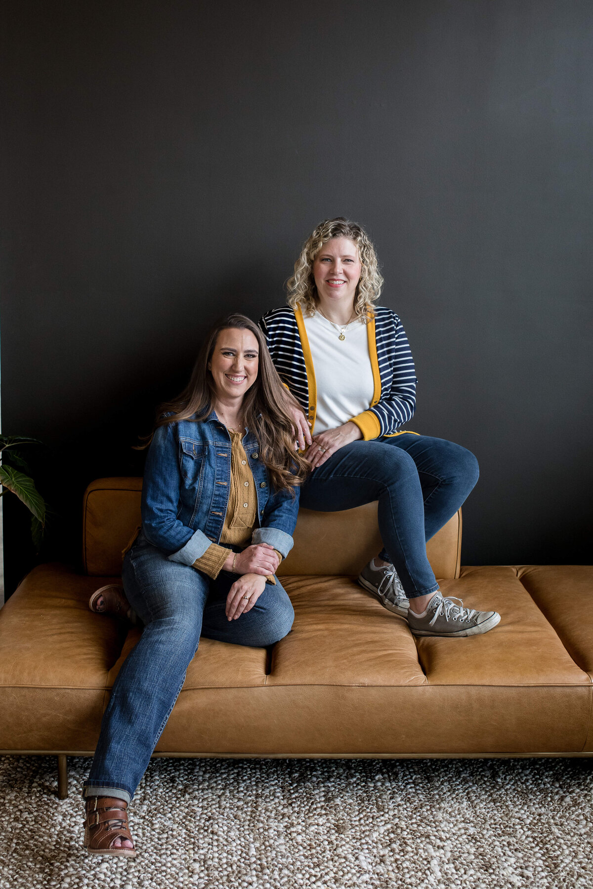 brand photographer near me captures two business women sitting on a brown leather sofa and a studio session for brand photo shoot in Orlando