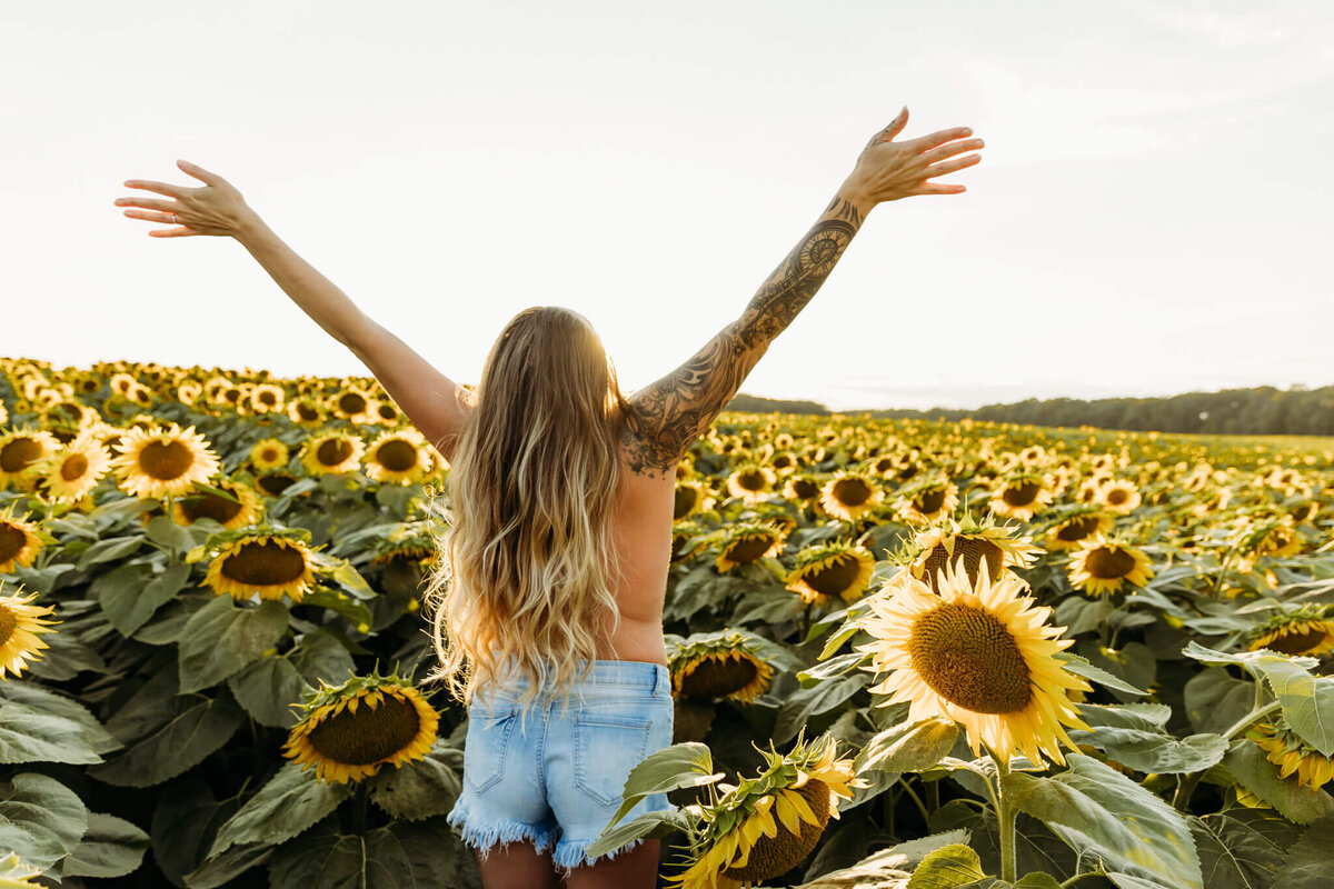 woman standing topless in a field of sunflowers for a boudoir session