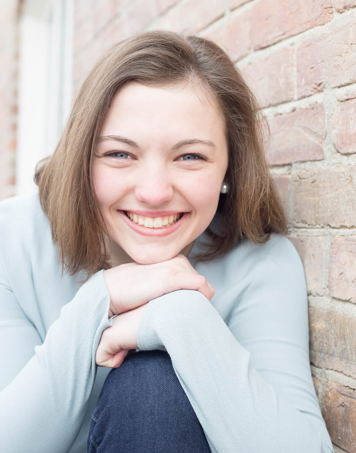 brown haired senior girl wearing a light blue shirt smiling with head on hands on knee