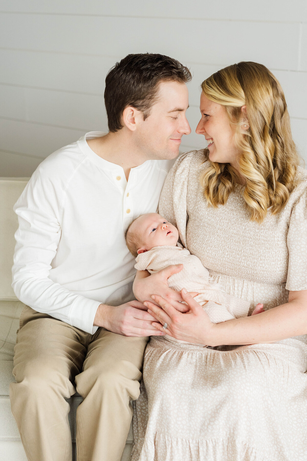 mother and father look lovingly at one another while newborn looks up at them