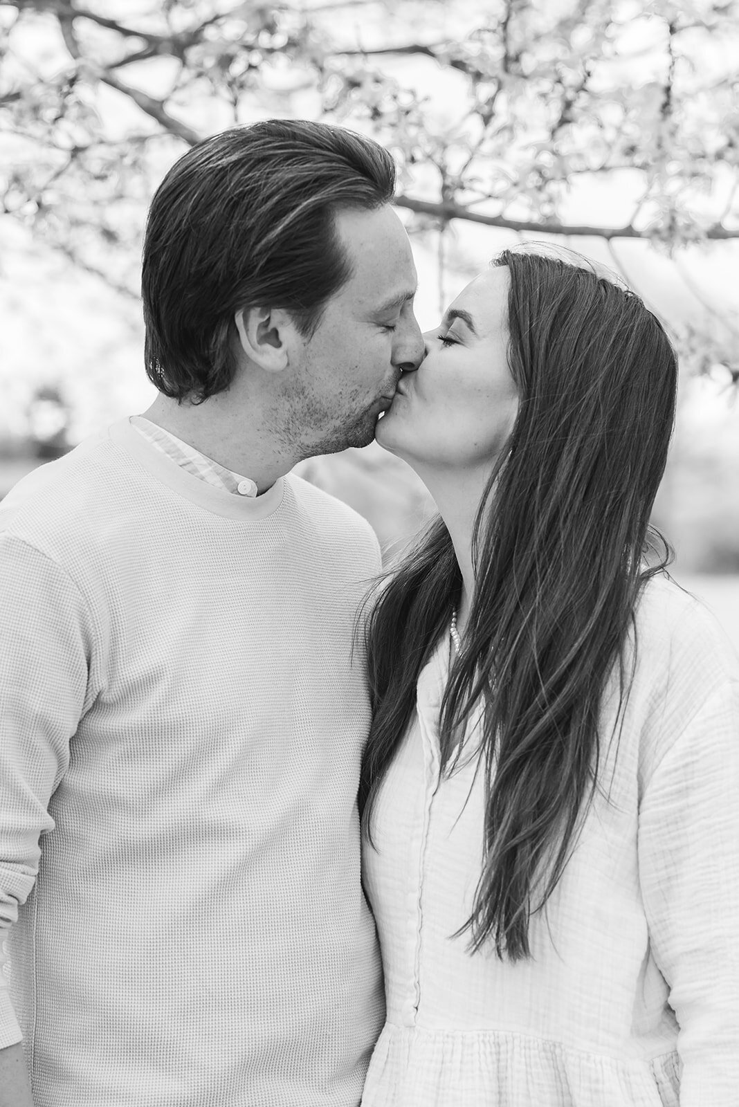 Black and white image of a coupel kissing under a blossom tree.