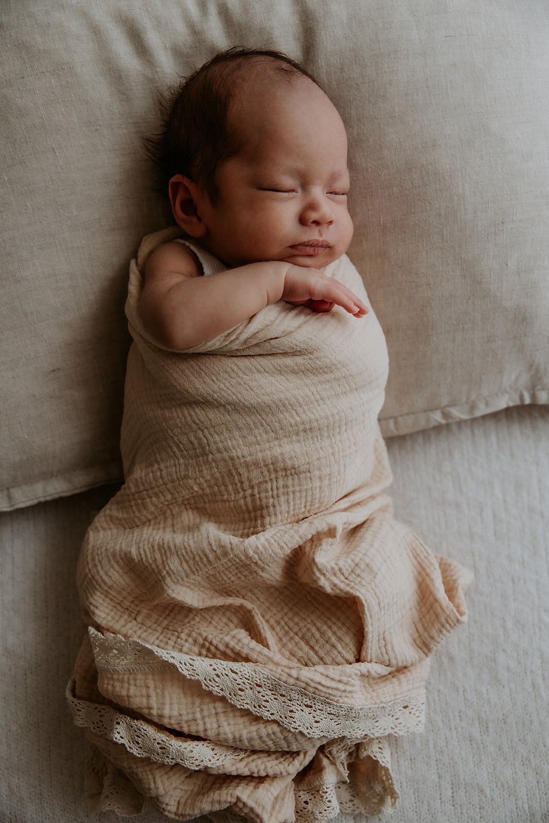 Newborn baby gilr wrapped in muslin and lying sleeping on cushion