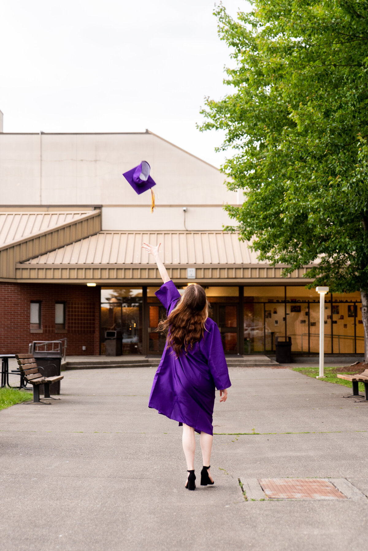High school senior girl facing away from the camera in her cap and gown, tossing her cap in the air over her head