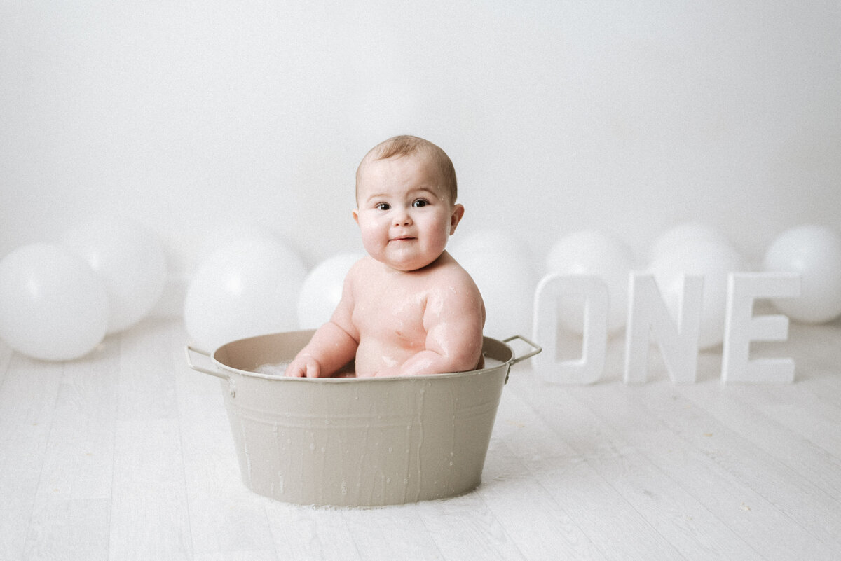 baby boy sitting in a tub smiling at cake smash photoshoot in west sussex