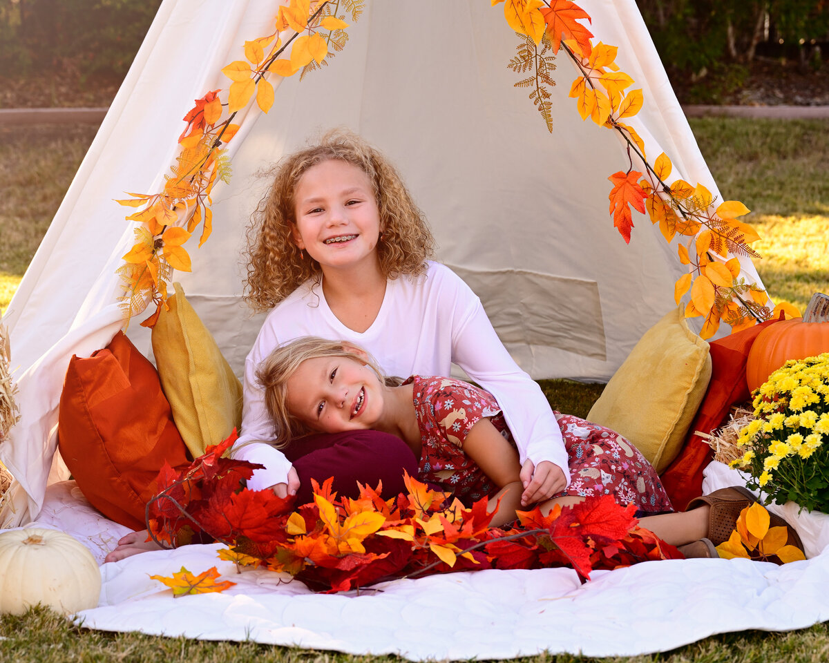 McKinney, TX family portrait session of two young  girls outdoors sitting in their tent with fall leaves and flowers.