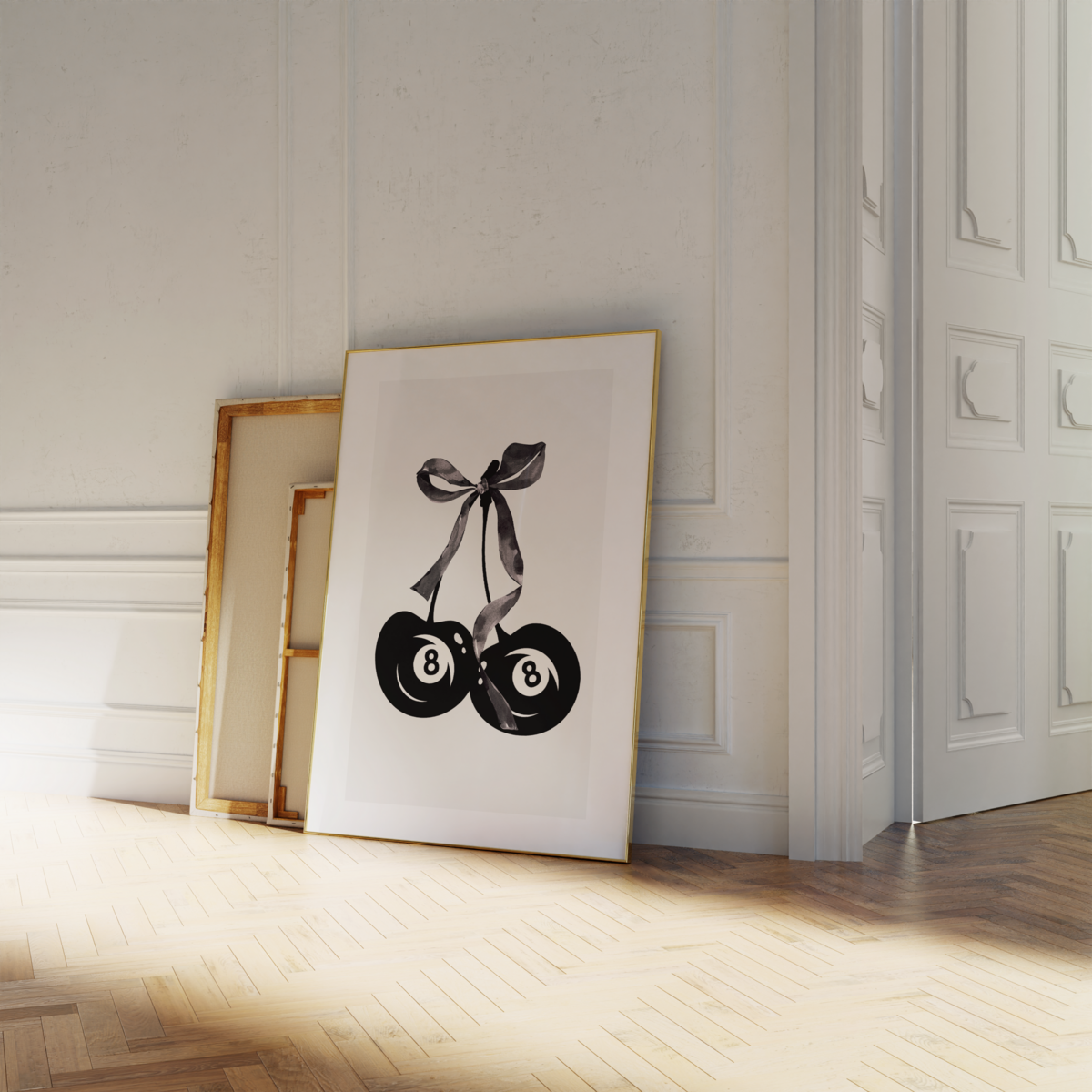 A framed artwork by Sweet Pea Ink Creative features two billiard 8 balls tied with a ribbon, leaning against a wall beside empty frames on a wooden floor in a brightly lit room—a perfect accent for any brand design enthusiast.