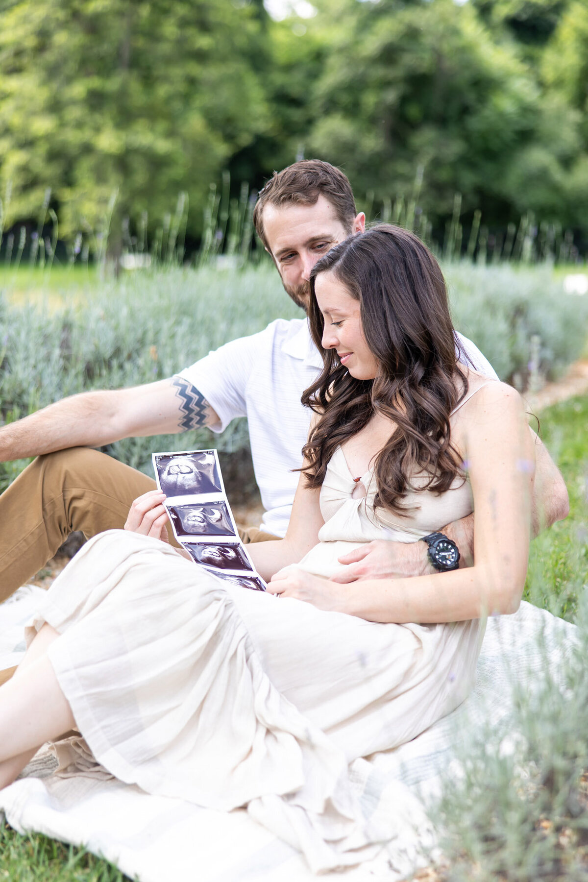 Soon to be parents sitting in a filed, looking at their ultrasound photo