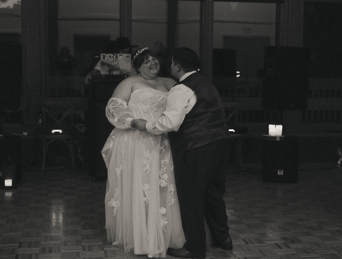A wedding couple smiles at each other and has their first dance at their wedding reception.