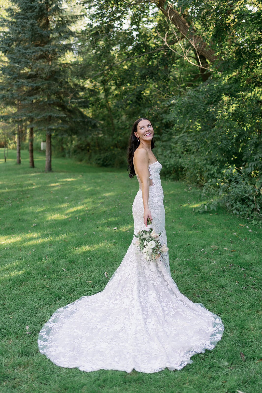 Bride in a lace strapless wedding gown standing in the garden at Glasshouse Community during a summer Michigan wedding.