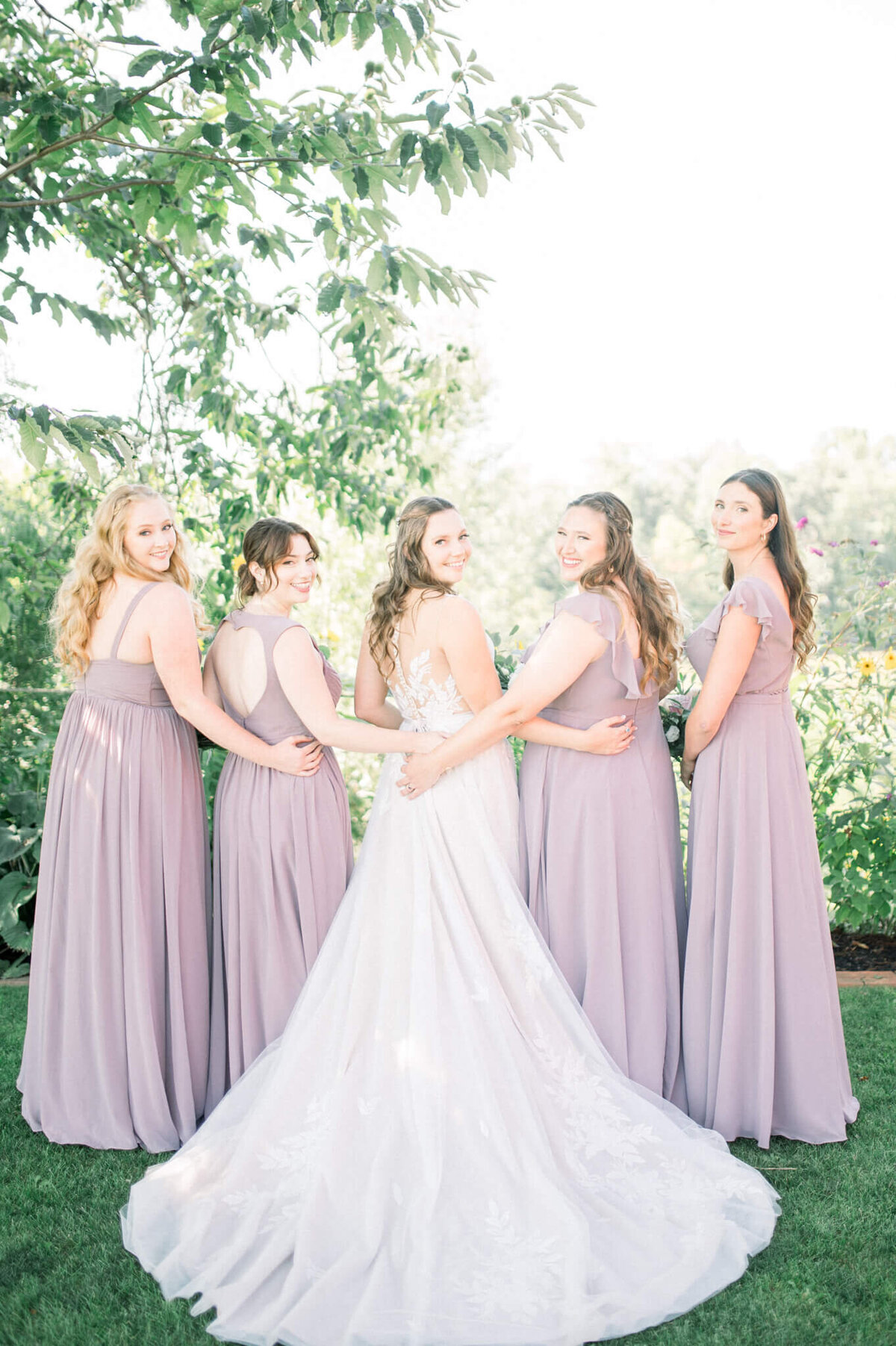 Bridesmaids and bride show off the back of their dresses to their Toronto wedding photographer